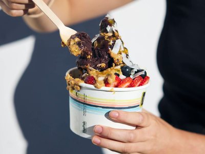 An açai bowl topped with strawberries, blueberries and peanut butter, held in front of a navy and white wall