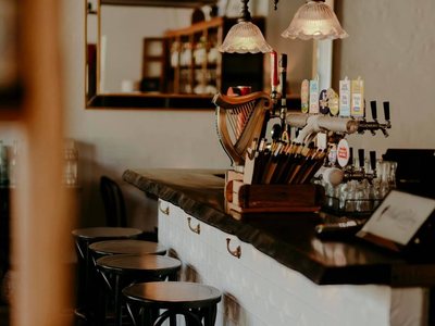 A bar with a dark timber top, beer taps and a row of bentwood stools, under glass pendant lights