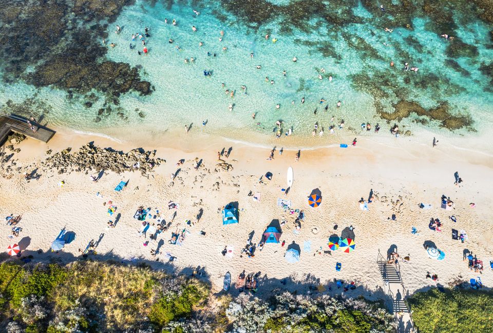Mettams Pool from directly above: swimmers in a turquoise lagoon inside the reef, and umbrellas on white sand