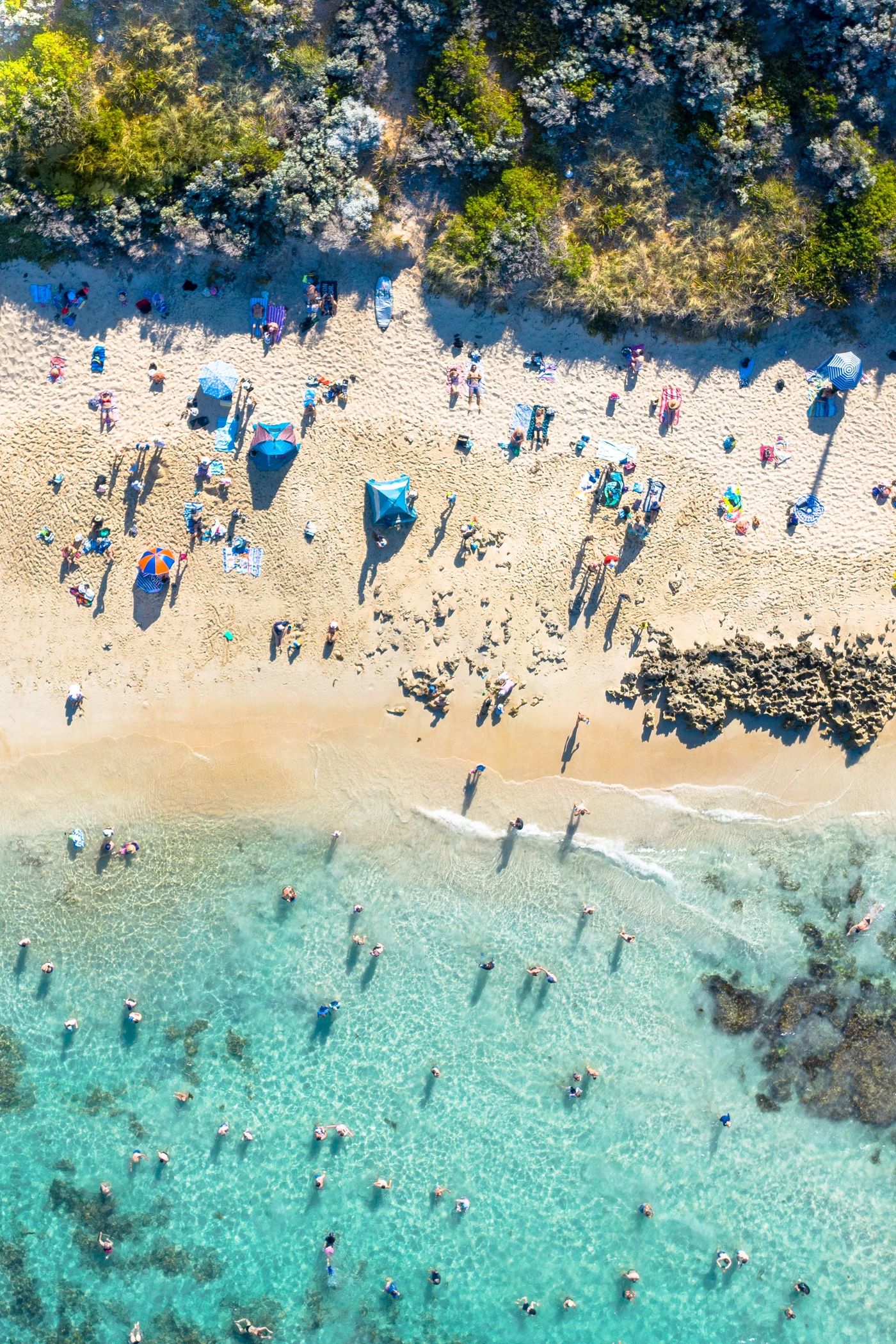 The shoreline at Mettams Pool from above: umbrellas on the sand and swimmers in clear shallow water
