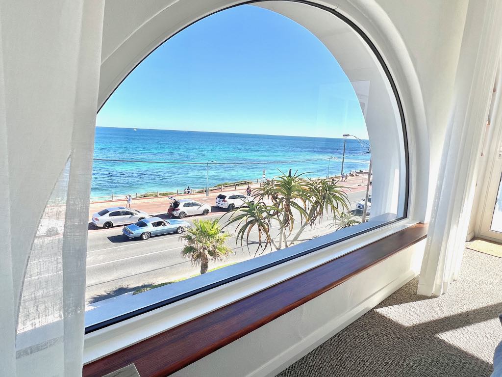 Arched window with a timber sill looking over the coast road to turquoise water