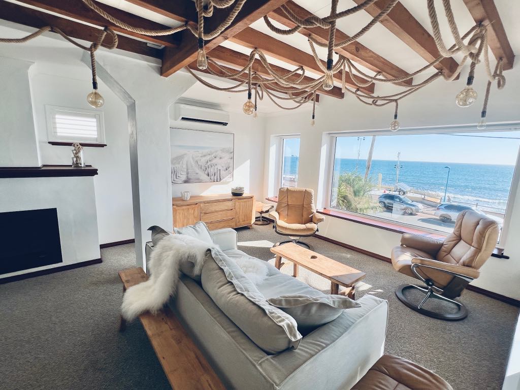 Living room with exposed timber beams, rope lighting, a linen sofa and a picture window facing the ocean