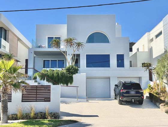 The white rendered house from West Coast Drive, with an arched window on the top floor and two garage doors