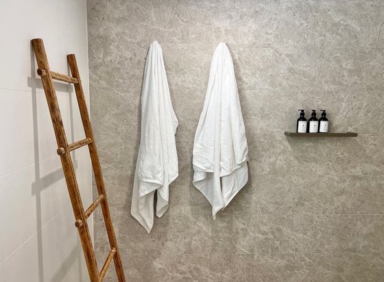 White towels hanging on stone tile beside a timber ladder
