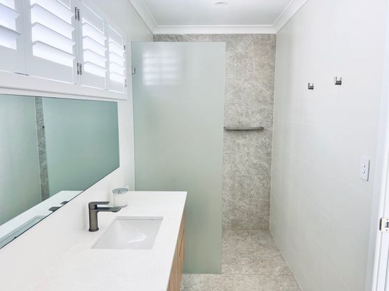 Bathroom with a timber vanity, shutters and a walk-in shower behind frosted glass