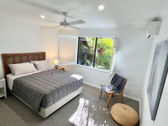 Bedroom with a cane bedhead, ceiling fan and a reading chair by the window