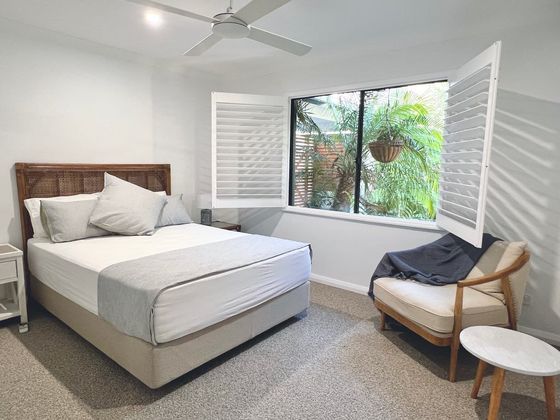 Bedroom with a cane bedhead, armchair and shutters open to a palm