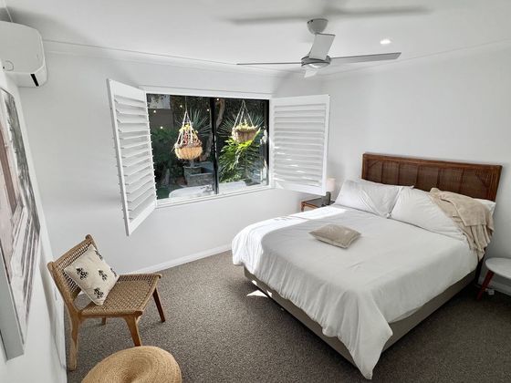 Bedroom with a cane bedhead and white shutters opening to hanging baskets in the garden