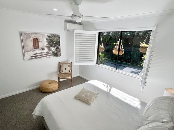 White bed beside shutters open to hanging baskets and the garden