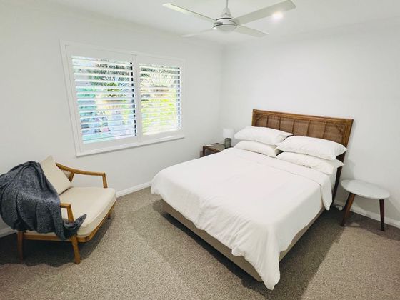 Bedroom with white linen, a cane bedhead, an armchair and a ceiling fan