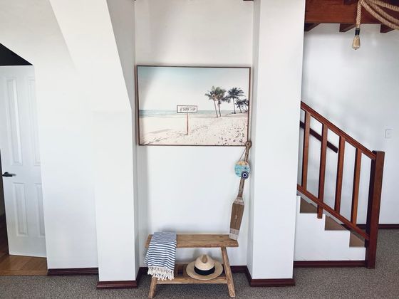 Bench with a beach towel and hat beneath a beach print, beside the timber staircase