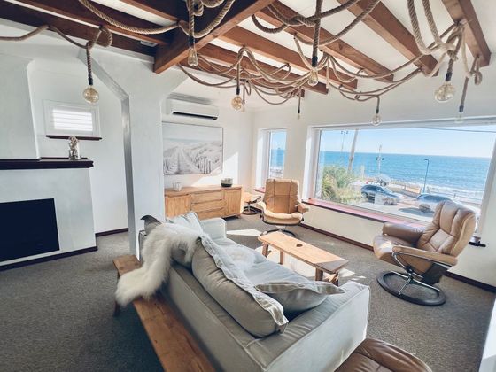 Living room with exposed timber beams, rope lighting, a linen sofa and a picture window facing the ocean