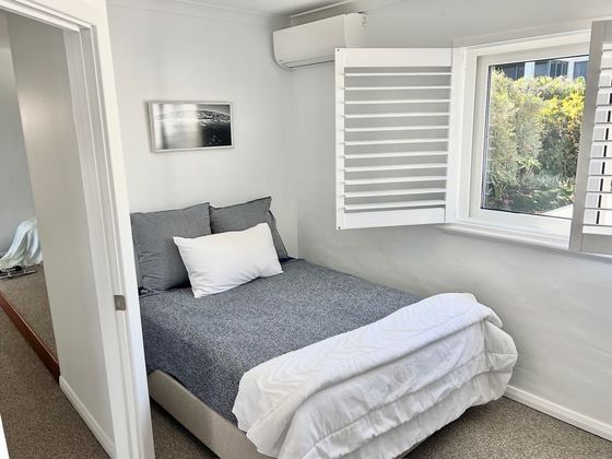 Double bed beneath a window with white shutters open to greenery
