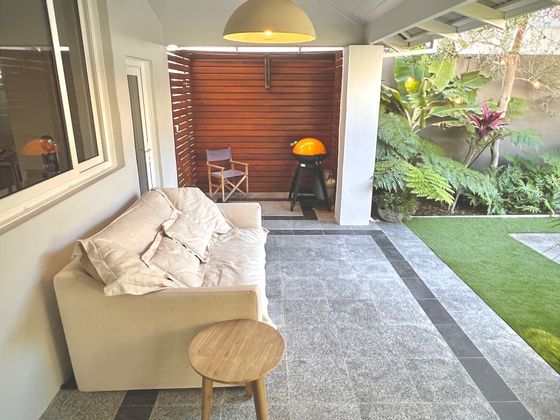 Covered terrace with an outdoor sofa, timber screen and barbecue, looking onto the garden